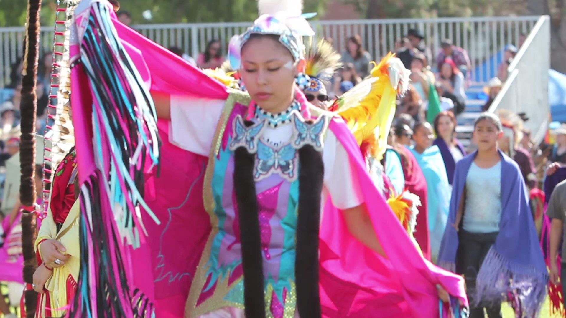 putaria telegram - A dancer in a bright pink shawl with fringe, wearing traditional regalia adorned with blue and black accents, performs at an outdoor cultural event.